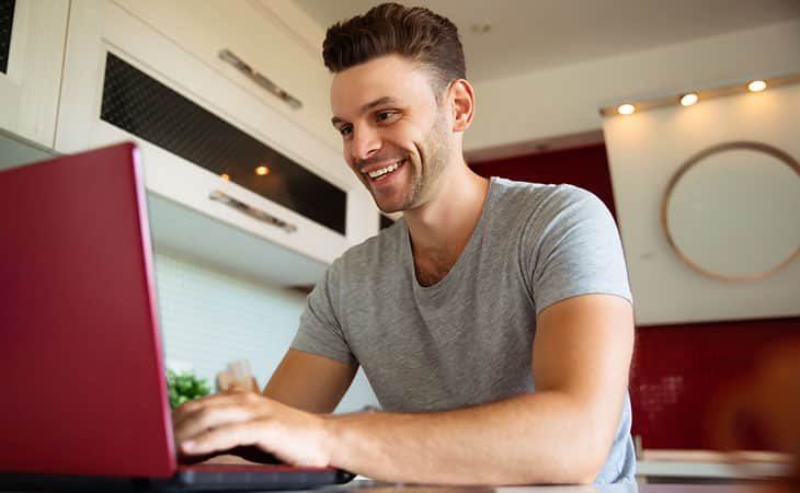 smiling-man-using-laptop-kitchen