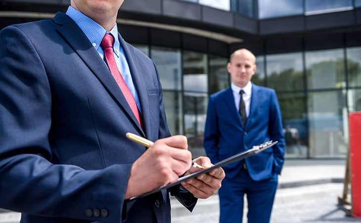 detail of a man is taking notes and man is behind him