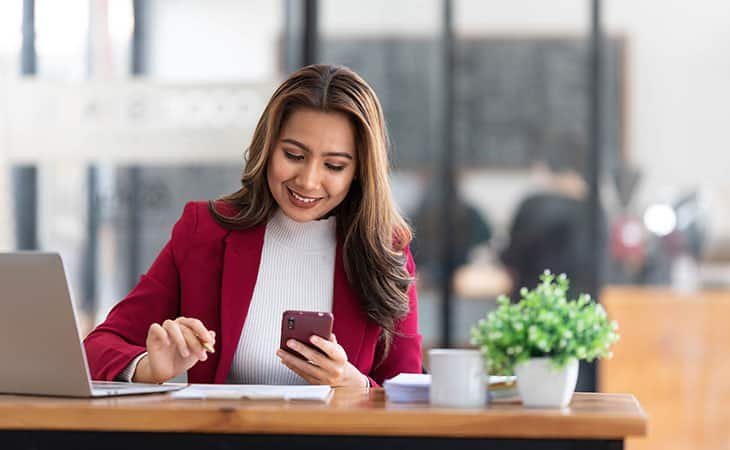 woman smiling using a smartphone seated at a table