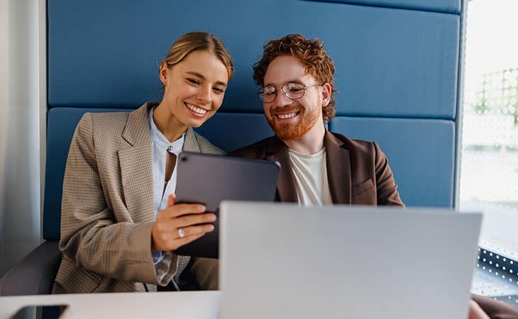 a businessman and a businesswoman smiling looking at a tablet