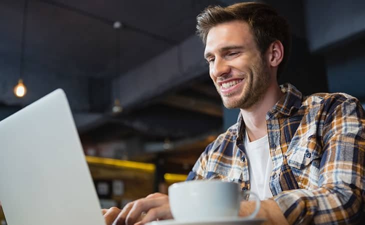 smiling young man looking at a laptop at a cafe