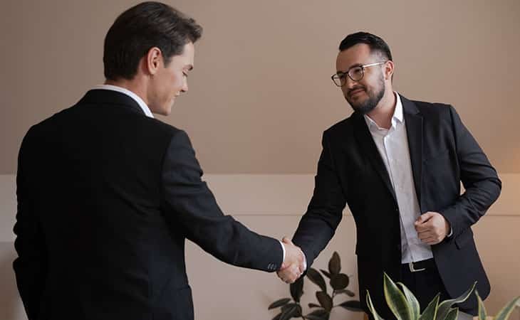 two men sheking hands smiling in a room with plants