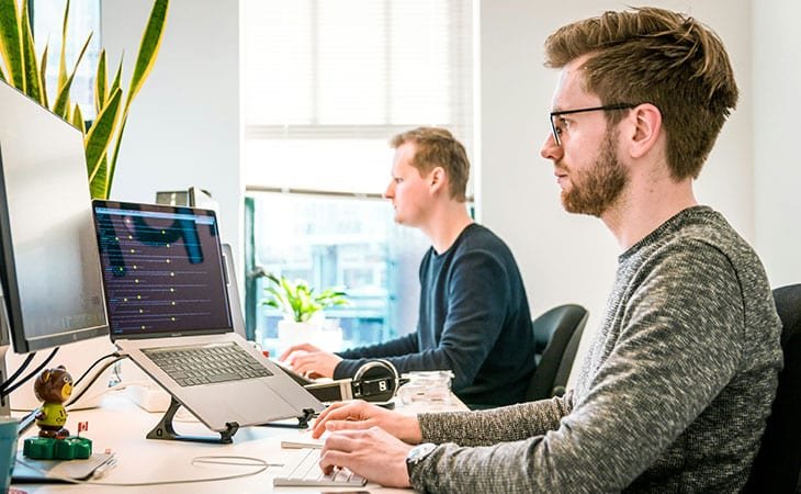 two men working with computers close to a window
