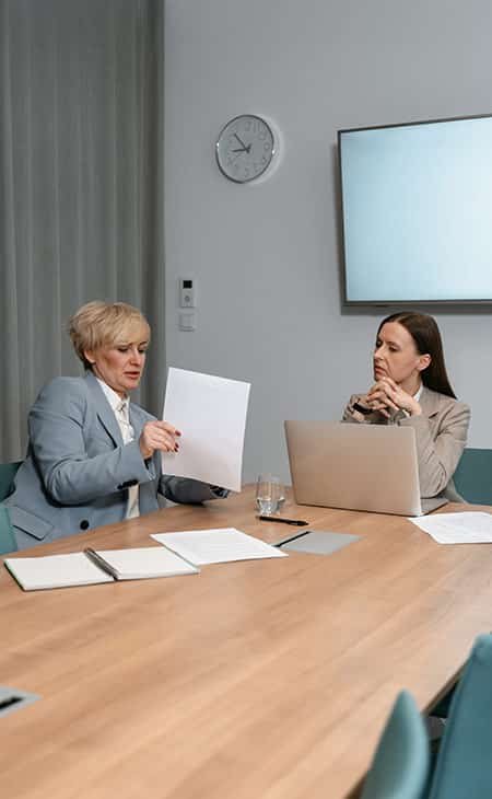 two women talking pointing to papers and using a laptop