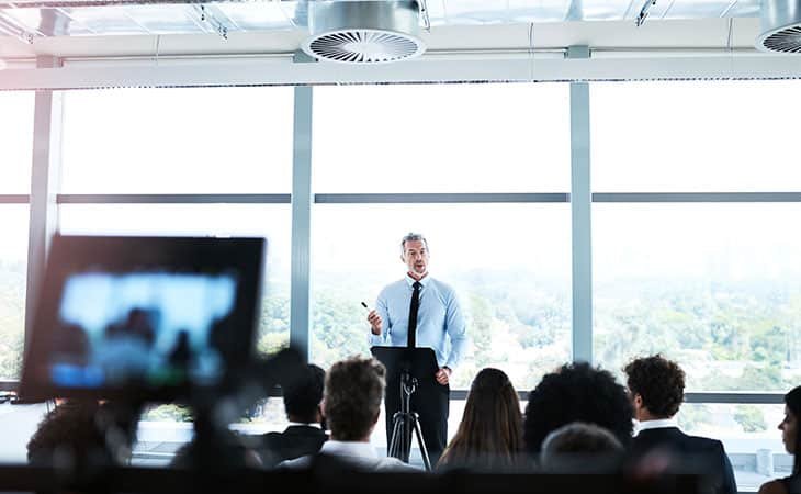 a man giving a speech to people in a workshop