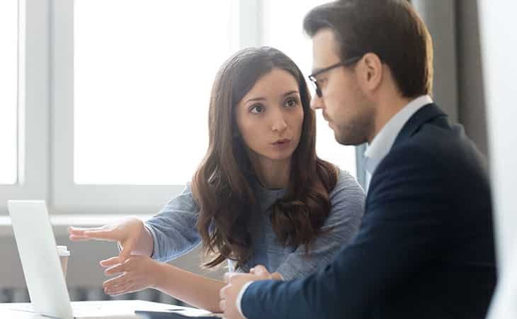 a woman talking to a man and pointing at a laptop screen