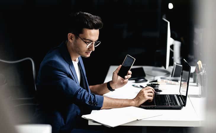 man-glasses-holding-phone-laptop