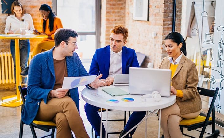 three people at a table and two people in the back of an office