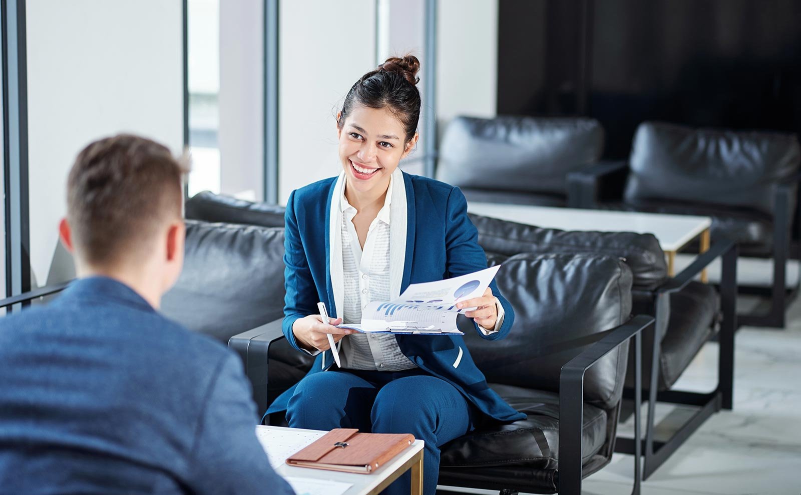 a smiling woman holding papers and looking at a man
